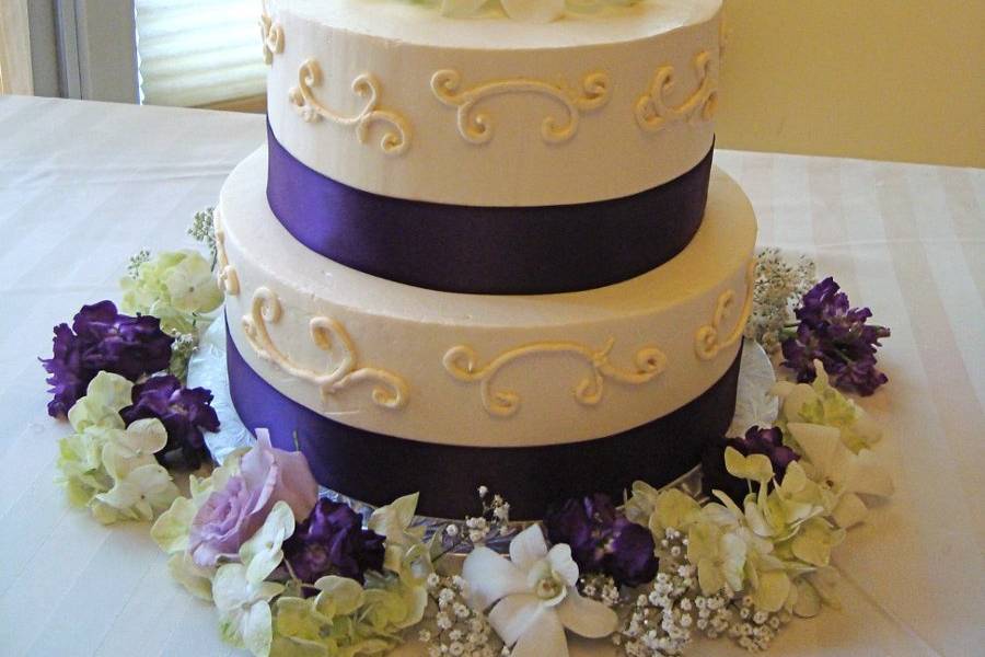 Ivory Wedding Cake with scroll work and purple ribbon.  Live flowers on top and around the cake.
