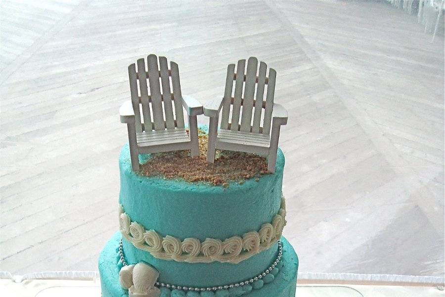 Teal beach cake with white chocolate shells, piped waves and wooden beach chairs as a topper.