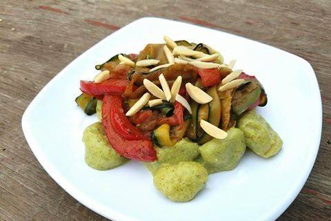 Creamy pesto gnocchi with roasted vegetables and garnished with almonds.