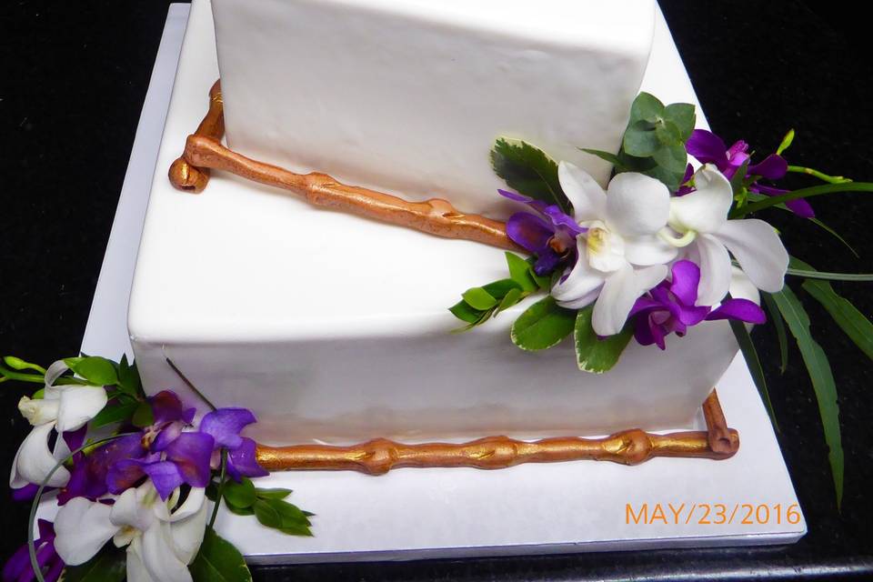 2 tier offset square fondant cake with sugar bamboo and fresh purple flowers and greenery.