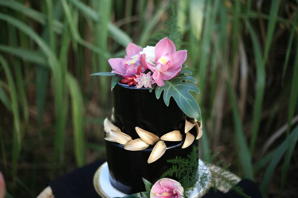 Two tier black cake with gold sugar leaves, fresh orchid and flower topper
