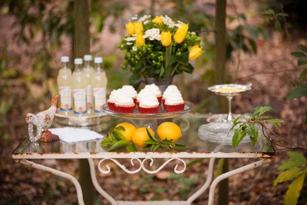 Antique table with vintage decor elements holding lemon cupcakes and French lemonade and a sterling silver heirloom footed candy dish with lemon candies.