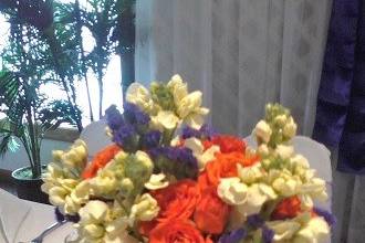 Orange spray roses, stock & purple statice with criss cross wrapped stems attendant bouquet by Loeffler's Flowers
