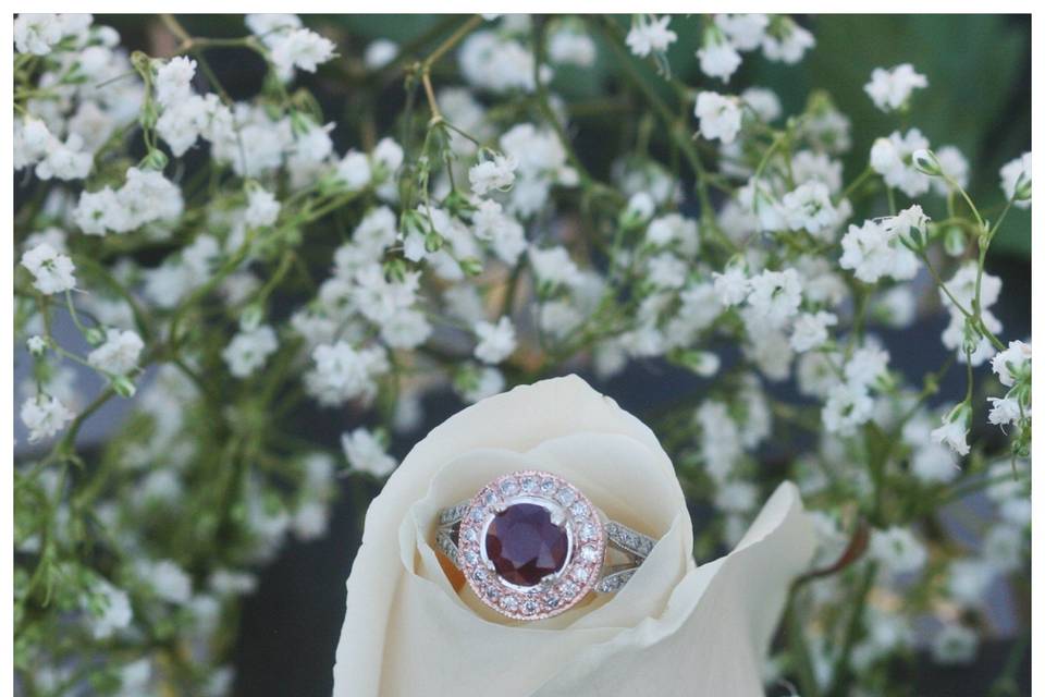 The star of this picture is this magnificent ruby engagement ring, set in rose gold and white gold, and surrounded by a diamond halo!
See full details here:
https://www.lauriesarahdesigns.com/product/ruby-and-diamond-ring-in-rose-and-white-gold-split-shank-%C2%97-ls415/