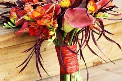 This artistic bouquet is made up of calla lilies,ranunculous, lilies, freesia, billy balls, protea, interesting foliages, copper crystal beaded strands and eggplant dyed feathers.  It is wrapped in a vibrant orange ribbon with copper wire detail.