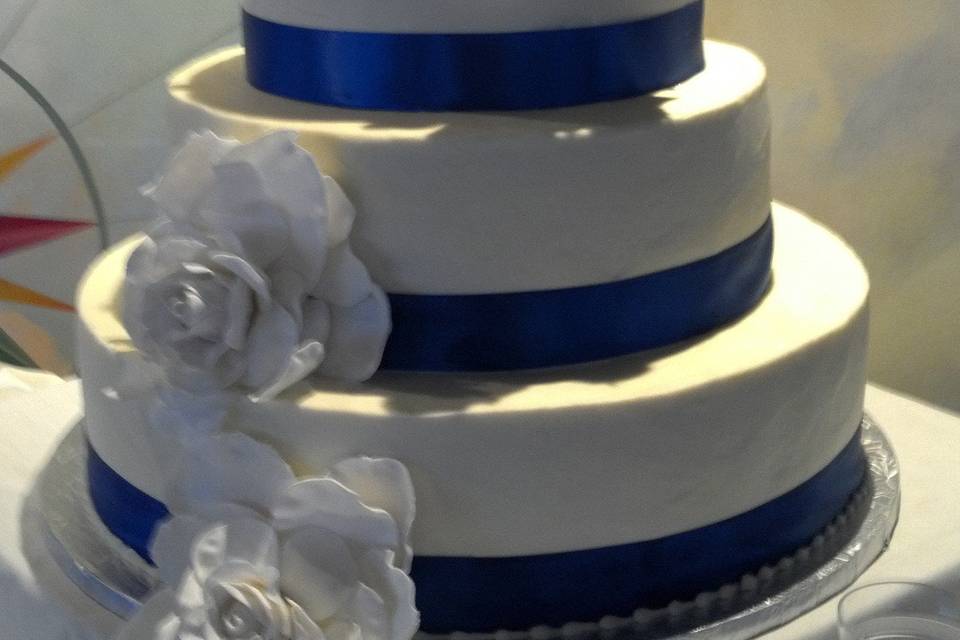 4 tier round wedding cake with sugar roses and royal blue satin ribbon.  The buttercream is iced so smooth it looks like fondant!