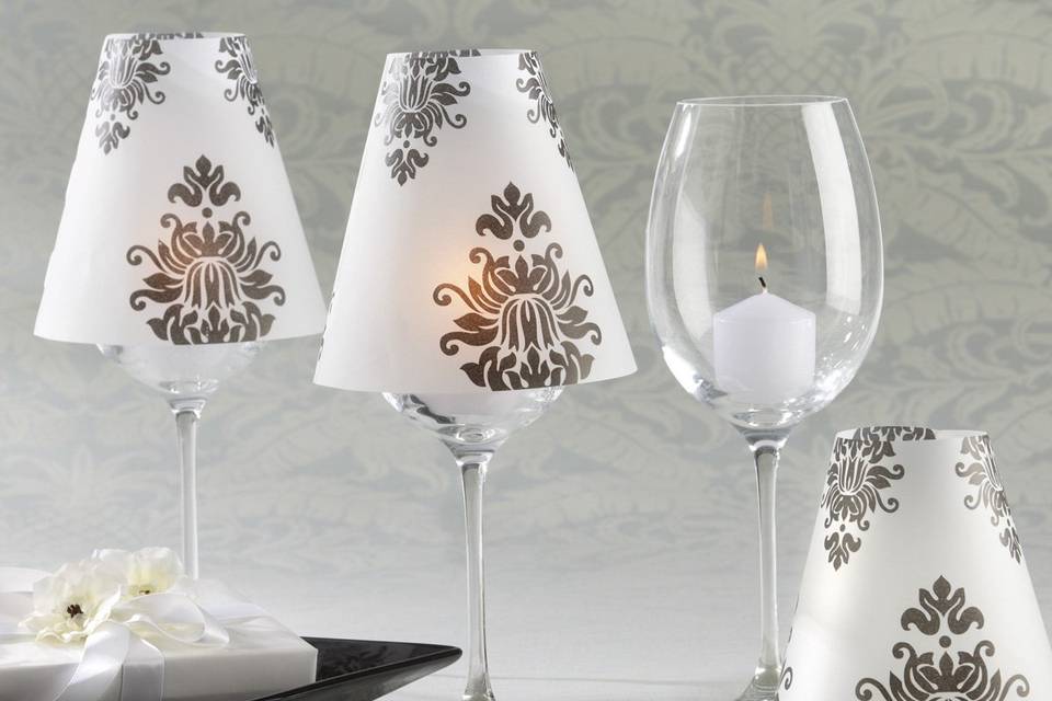 Introducing a new standard in elegant table decor! These exquisite black-and-white Damask Vellum Shades will create a mesmerizing glow throughout your reception hall or special event.
Details about these amazing favors:
- Classic black-and-white damask pattern adorns a translucent, vellum shade
- Shade fits on standard wine glasses to create a softly glowing table lamp
- Assembled shade measures approximately 4 3/4