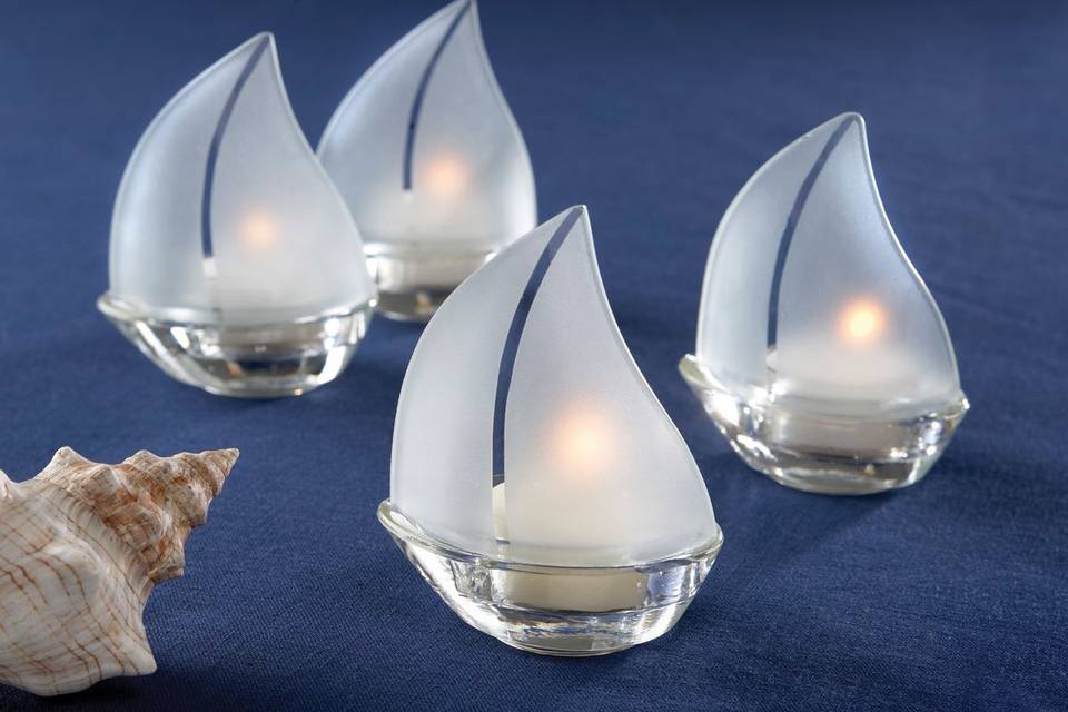 Perfect for a beach wedding or a function by the sea.  What Is more romantic image than candle-lit sailboats on a nighttime harbor, each one glowing with ambiance? These charming tealight holders make an impeccable presentation at every place setting, as the tealights within illuminate their frosted glass sails. They work great with springtime, summertime, or nautically themed weddings, especially. Sold in sets of four tealight candles included. Each sailboat measures 3