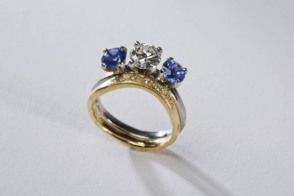 Diamond Platinum with Sapphires:  $7,200.00- $8,500.00
A Lovely Placement with the 1.10 ct. S1-H center Diamond, two high quality brilliant Blue Sapphires .80ct. & .84ct. adorned on a platinum band.  Partner with a Gold or white Gold diamond Pave' Band meticulously fit.  Both for $8489.00.