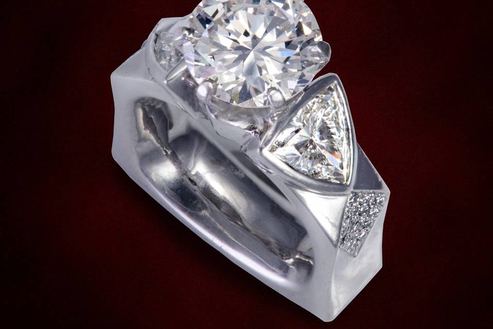Round brilliant cut diamond accented with trillions set in bezels with pave set diamonds.  A bold design accenting all the angles.