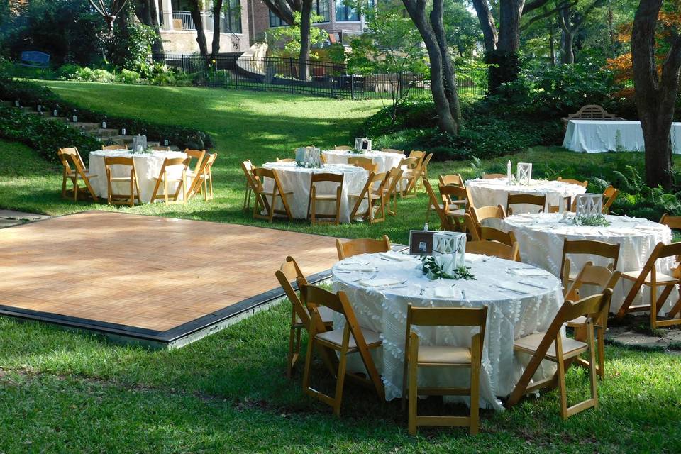 Backyard wedding ceremony and reception. Shady, grassy at-home comfort. Natural wood dancefloor and chairs, white linens and flowers.