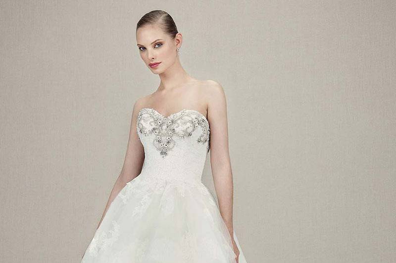 Style Kylee <br> Full-length ball gown of beaded embroidered lace, Alencon lace, and Chantilly lace. Adorned with silver beaded appliqués on sweetheart neckline bust. Tiered tulle layers cascade down from low V-back.