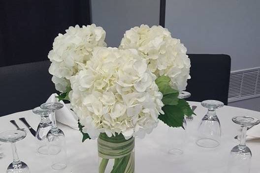 Cylinder vase with white hydrangeas and a submerged aspidistra leaf.