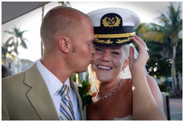 Groom kissing smiling bride wearing a captain's hat