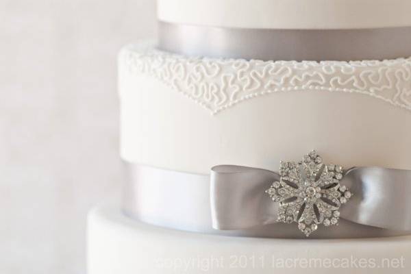 Piped lace detail and antique style brooches add elegance to this silver and white wedding cake