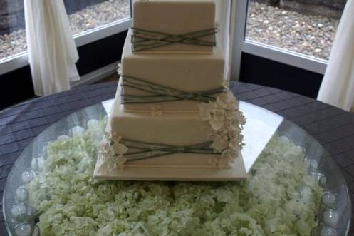 Silver ribbon and gumpaste hydrangea cake, displayed on elevated glass tabletop over candles and fresh hydrangeas