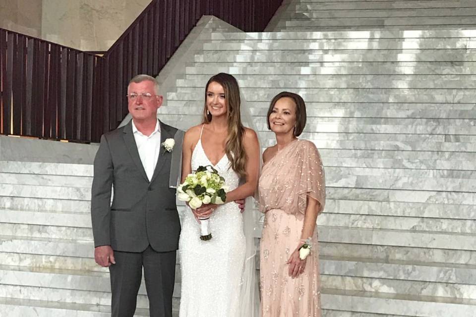 Mother of the bride wearing a one shoulder Adrianna Papell beaded dress in blush.