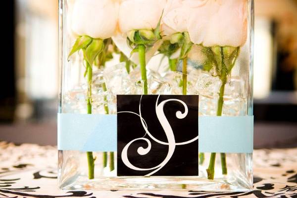 Rachel & Matt's wedding was designed around their wedding logo, created by the bride herself, also a graphic designer.
These centerpieces were pave style roses in cube vase wrapped with blue ribbon & finished with the logo. All set atop damask linens.