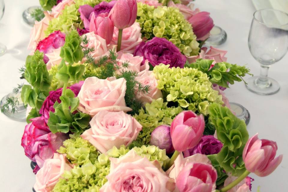 A series of low containers creates the illusion of one long arrangement of Tulips, hydrangea, and roses