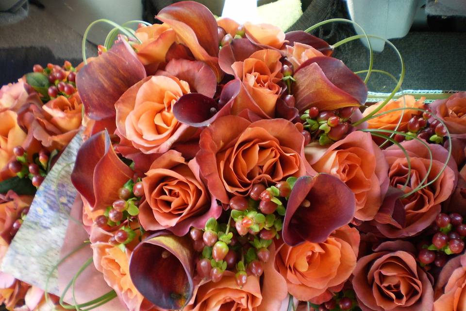 Orange and rust roses, rust mini callas, hypericum berries with bear grass accents