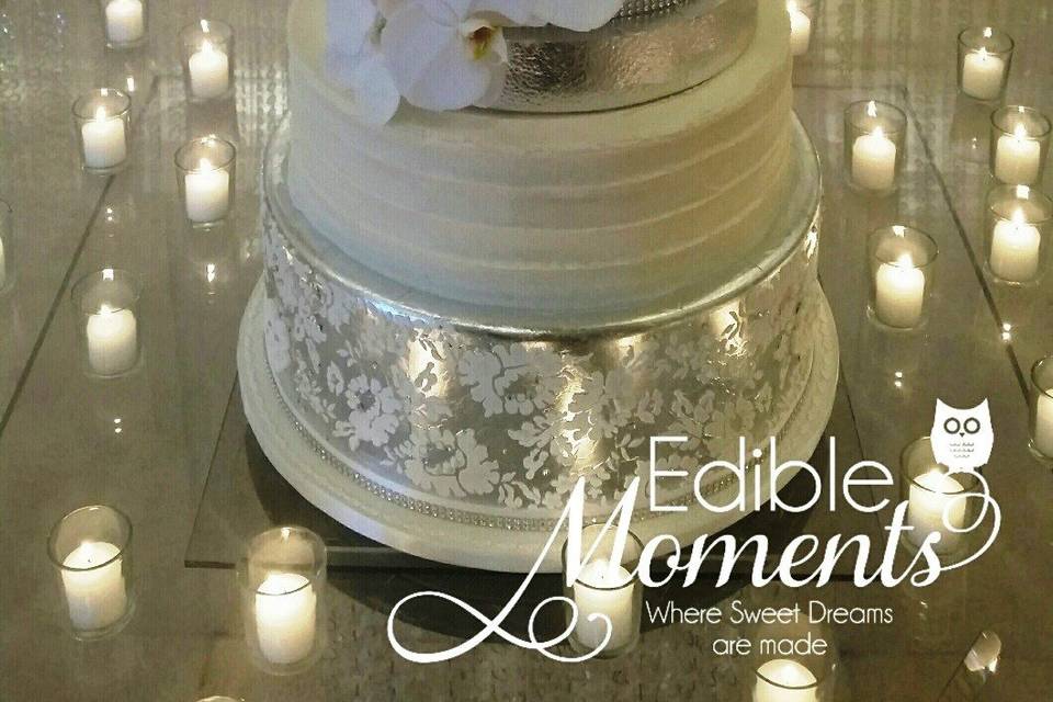 7-tier Chic Romantic Silver & White Wedding cake.  Edible lace on top 2 tiers adorned with Swarvoski crystals & pearls.  Edible silver leaf separator tiers.  Fresh orchid flowers.  Butter cream tier. Bottom tier covered in edible silver leaf with a stencil overlay design adorned with Swarvoski crystals & pearls.  Stunning.