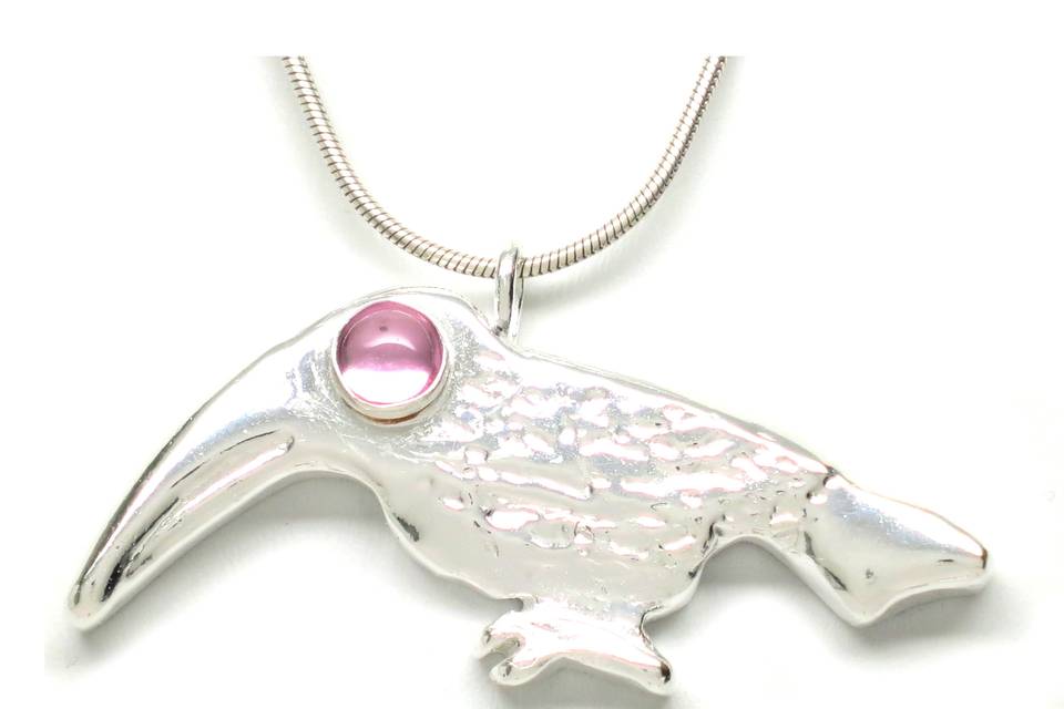 Sterling Silver Toucan Pink Sapphire Cabochon Pendant Necklace The artistically unique style of the sterling silver pink sapphire toucan necklace is a work of art in its own right. Heavy and substantial with a cabochon set lab grown pink sapphire eye. Finished in a high polish,  it measures 1 inch high by 2 inches wide by 1/4 inches deep. The sterling silver toucan is suspended with a ring and showcased on an 18-inch sterling silver snake chain with a lobster clasp. The toucan necklace is a high fashion piece that connotes a bold statement of celebrity and notoriety. The pink sapphire is 6mm round, lab-created.Symbolism: Toucans represent paradise and peace. The toucan has a colorful appearance and large bill, indicating a strong desire to be seen and heard. Toucans refer to the importance of teamwork and family, partnership and companionship.