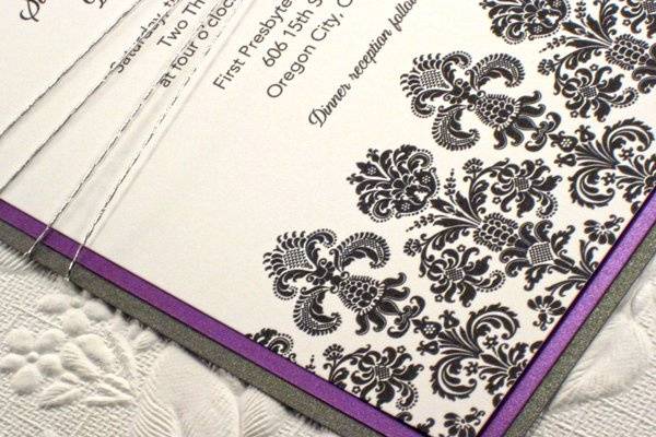 This distinctive wedding invitation is adorned along the bottom with a wide damask band with a velvet appearance. Invitation is printed on 130lb cardstock, adorned by a silk metallic purple layer, and a final silver backing layered. Final product was wrapped in a silver hemp.