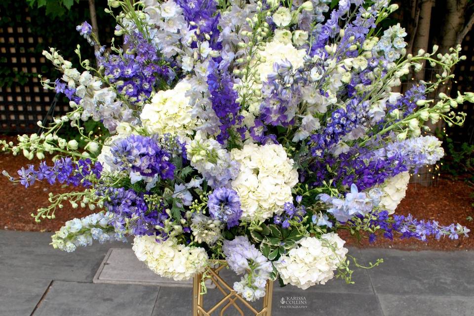 Lush summer flowers on gold metal pedestal for courtyard ceremony