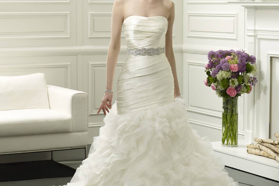 D8054
The fitted, strapless bodice softly dips into a sweetheart neckline and is ruched asymmetrically. The fit and flare gown features layers of soft organza that folds into the asymmetric skirt. Finished with an optional sash 