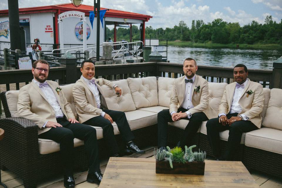 Groom & groomsmen in the outdoor lounge on The River Room's Riverfront Deck in historic downtown Wilmington, NC. Furniture and accessories provided by Custom Home Staging & Design. Ceremony. Photo by Lightbloom Photography.