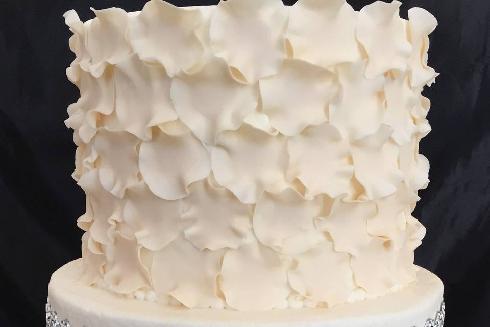 An ivory elegance! Handcrafted sugar petals create a textured look on this buttercream cake while a non edible glam band makes it stylish!