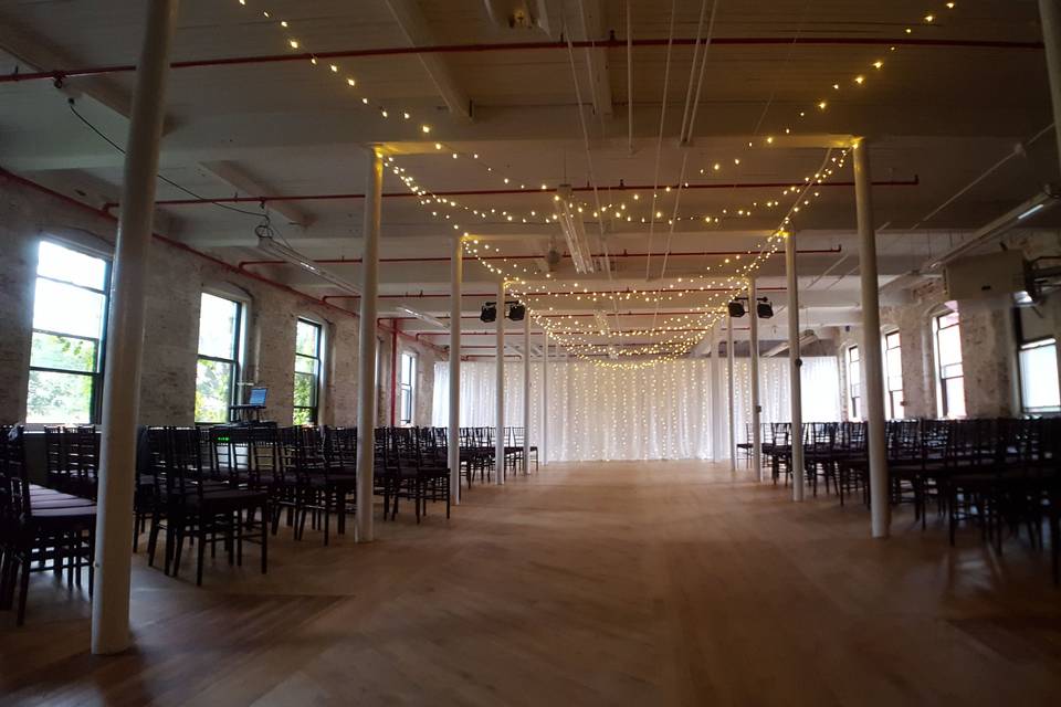 A large multi-layered twinkling backdrop and string lighting from the ceiling over the aisle for a wedding ceremony in the South Room of the Stationery Factory.