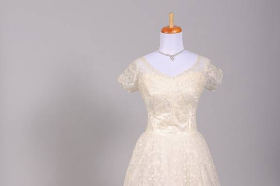 1950's Floral Lace Vintage Wedding Gown
Designed in the 50's this special vintage wedding gown is done in a floral embroidered net over silk with an additional two layers of tulle in the skirt. The bodice offers a scalloped trimmed scooped neck line v-cut back and capped sleeves which are slightly gathered at the shoulder. The silk lining can be seen through the sheer embroidered net and features a sweetheart neck line and back. The full and gathered skirt falls from the Basque style waist and offers a sheer floral embroidered net panel in the front and in the back where a self train is seen.
http://www.millcrestvintage.com/vintage-wedding-dresses/1950s-floral-lace-vintage-wedding-gown