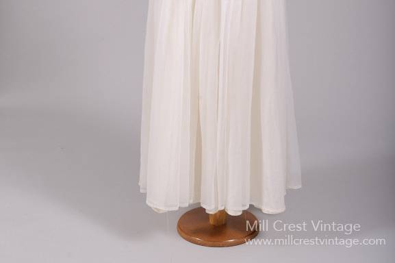 1960's Chiffon Rhinestone Vintage Wedding Gown
Designed in the 60's, this beautiful vintage wedding gown is done in a ruched white poly chiffon over an acetate lining. The bodice offers a scooped neckline, v-cut back and capped sleeves. The full and gathered skirt falls from the self banded ruched cumber bun waist, which features with two rhinestone adornments at the hips. A concealed nylon zipper and two hook n'eyes enclose this gown in the back.
http://www.millcrestvintage.com/vintage-wedding-dresses/1960s-chiffon-rhinestone-vintage-wedding-gown