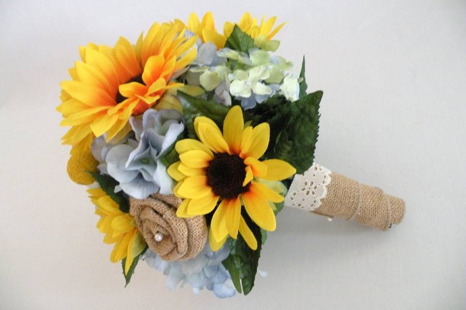 Shabby chic and romantic, this quality silk bouquet is created with light blue hydrangea, yellow sunflowers and burlap ribbon roses.  The handle is wrapped in a burlap ribbon with a lace accent. This bouquet is available in other colors.