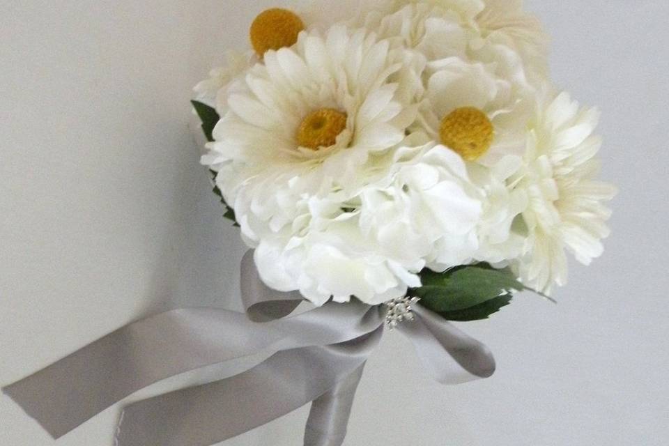 Shabby chic and romantic, this quality silk bouquet is created with white hydrangea, white gerbera daisies and yellow craspedia (billy balls).  The handle is wrapped in a silver gray satin ribbon and accented with a rhinestone brooch. This bouquet is available in other colors.