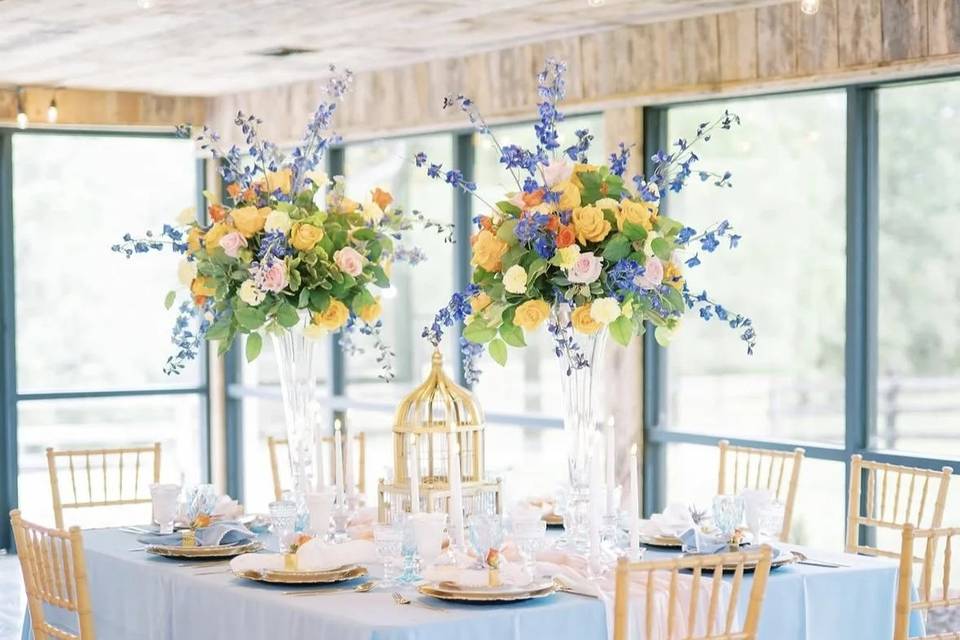 A reception table in blue and yellow florals beside the barn's glass wall