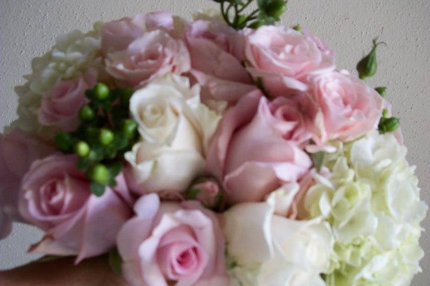 Round bouquet with a mixture of soft pink roses, ivory roses, green hypericum berries, and white hydrangea for a soft and sweet look.