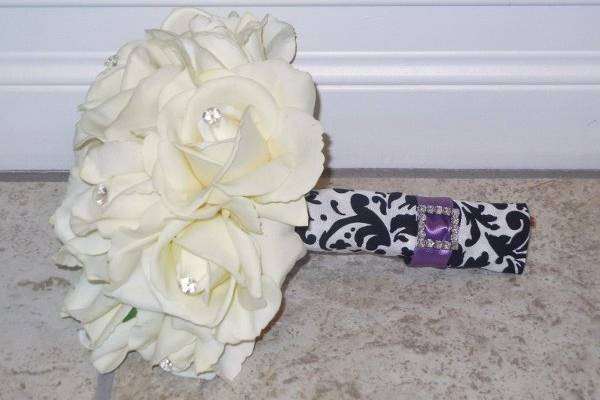 White Real Touch Roses w/ Rhinetones in the centers.  The stems are wrapped in Damask fabric with a rhinestone buckle and accented with purple ribbon.
