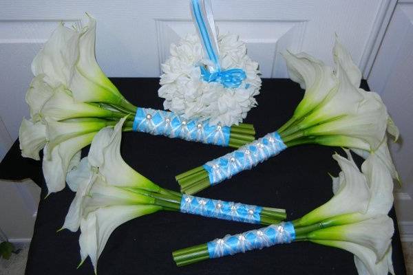 A wedding package with white silk calla lilies.  All of the bouquets are wrapped in blue satin ribbon and accented with white sheer ribbon and crystal pins on the handle.  The flower girl will be carrying a stephenosis ball with a blue and white handle.