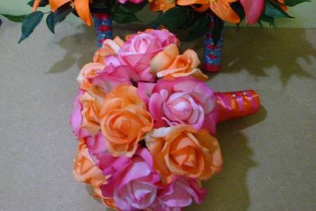 The bridal bouquet is hot pink & orange real touch roses and the stems are wrapped in hot pink ribbon accented with orange ribbon and pearl pins.  The attendant bouquets have orange lilies, hot pink calla lilies, orange and pink roses and orange filler flowers.  The stems are wrapped in hot pink ribbon and accented with blue.