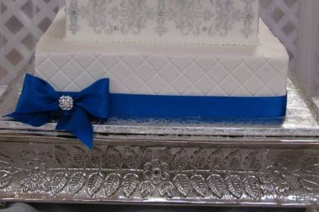 White buttercream icing with satin ribbon bows, fondant monogram, buttercream stenciling and fresh roses as topper.