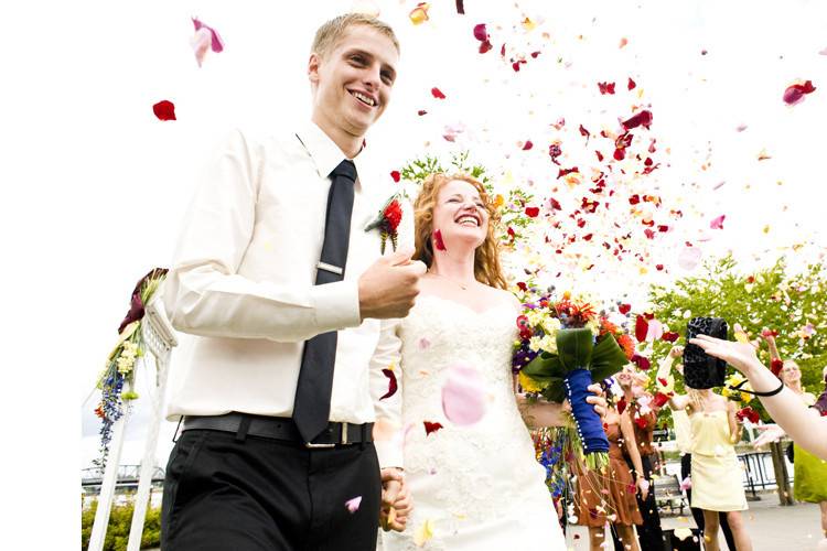 Happy newlyweds being showered with flower petals