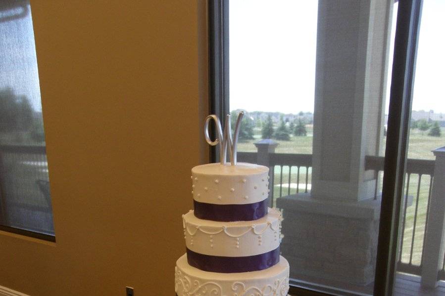 Tiered cake with buttercream icing and purple ribbon to accent.  Silk petals and votive candles provide additional beauty to the cake table.