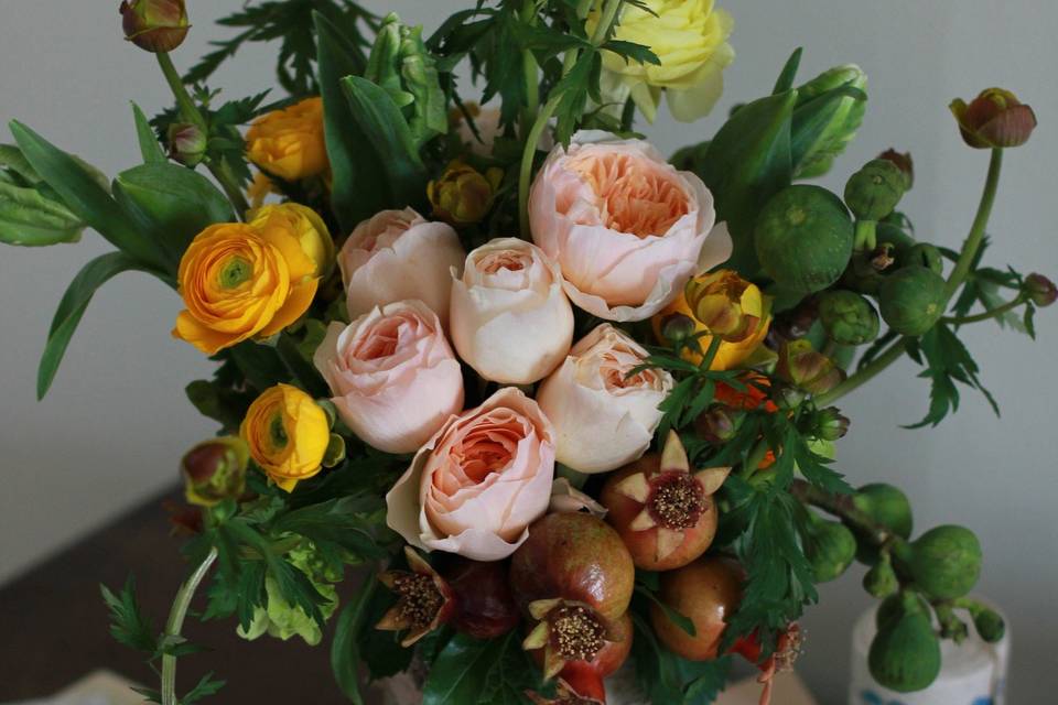 Custom floral arrangement in a rustic birch-bark vase filled with peach garden roses, pomegranates, fig branches, anemones & yellow ranunculus. SWOON!