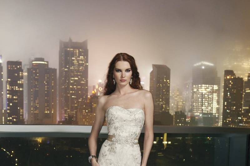 Style # 9747Charmeuse fit and flare gown featuring an asymmetric pleated sweetheart neckline, hand beading at empire waist and spaghetti straps. The low back is highlighted by crystal embellished yoke and the back is finished by charmeuse covered buttons over back zipper and a chapel length train.