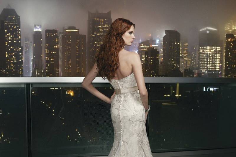 Style # 9747Charmeuse fit and flare gown featuring an asymmetric pleated sweetheart neckline, hand beading at empire waist and spaghetti straps. The low back is highlighted by crystal embellished yoke and the back is finished by charmeuse covered buttons over back zipper and a chapel length train.