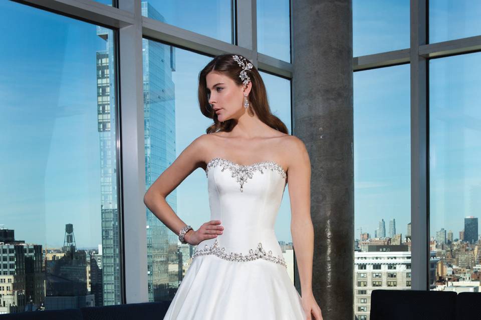 Style 9818 <br> You will be sure to make a fierce entrance with this high-low ball gown featuring corded embroidered lace on a nude illusion neckline, with soft handkerchief underlay and an illusion back.