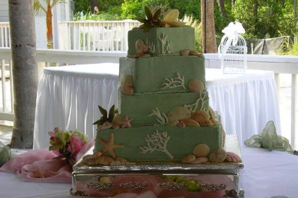 Butter cream covers this cake with a seaside theme, designed by the groom.  The flowers are handmade gumpaste, the sea shells are white chocolate and the pearls and rope trim are fondant.  All the coral pieces are piped with royal icing.  This cake served 225 guests.