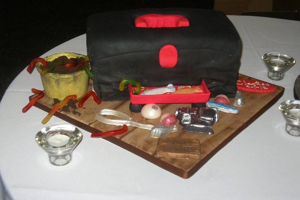 Tackle box is a fondant groom's cake with lures, worms, and bobbers.  This cake was red velvet, the grooms favorite.  The tools and hooks etc. were made by me of gum paste.  The board was fondant made to look like distressed boards of a dock.  His real tackle box is black and red.